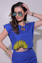 Woman wearing a blue dress with a yellow sunflower design, sunglasses, and bracelets on a plain background