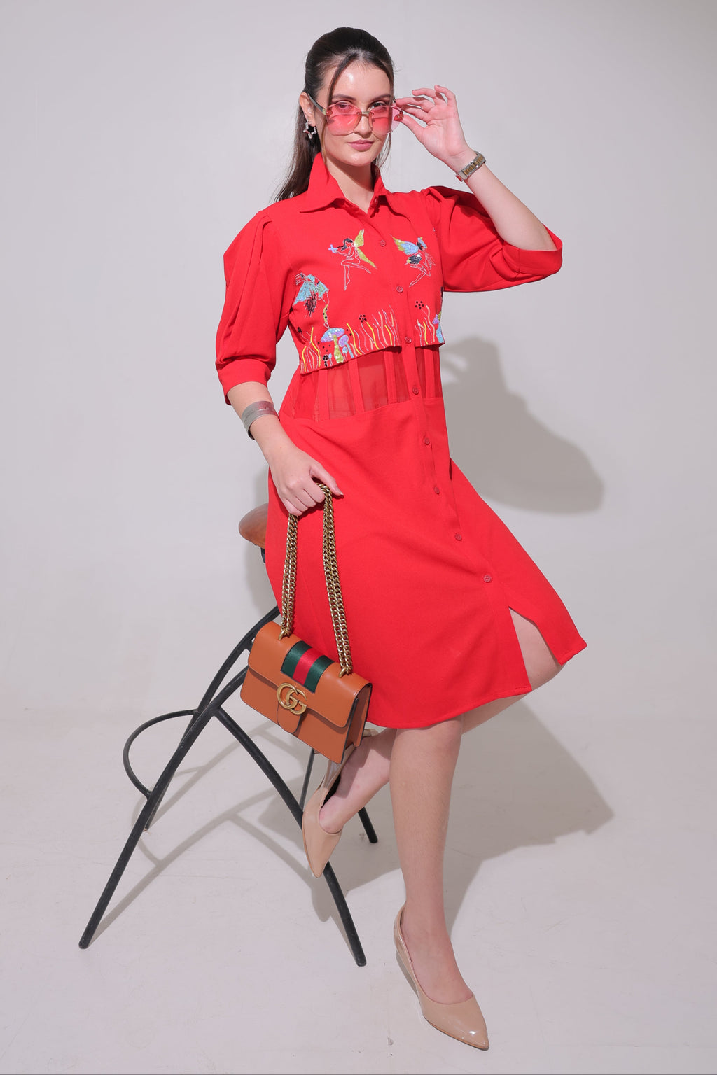A woman wearing a red dress with embroidery on a plain background