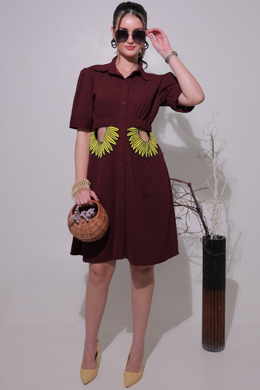 Woman in a maroon dress with yellow accents holding a woven basket on a plain background