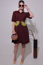 Woman in a maroon dress with yellow accents holding a woven basket on a plain background