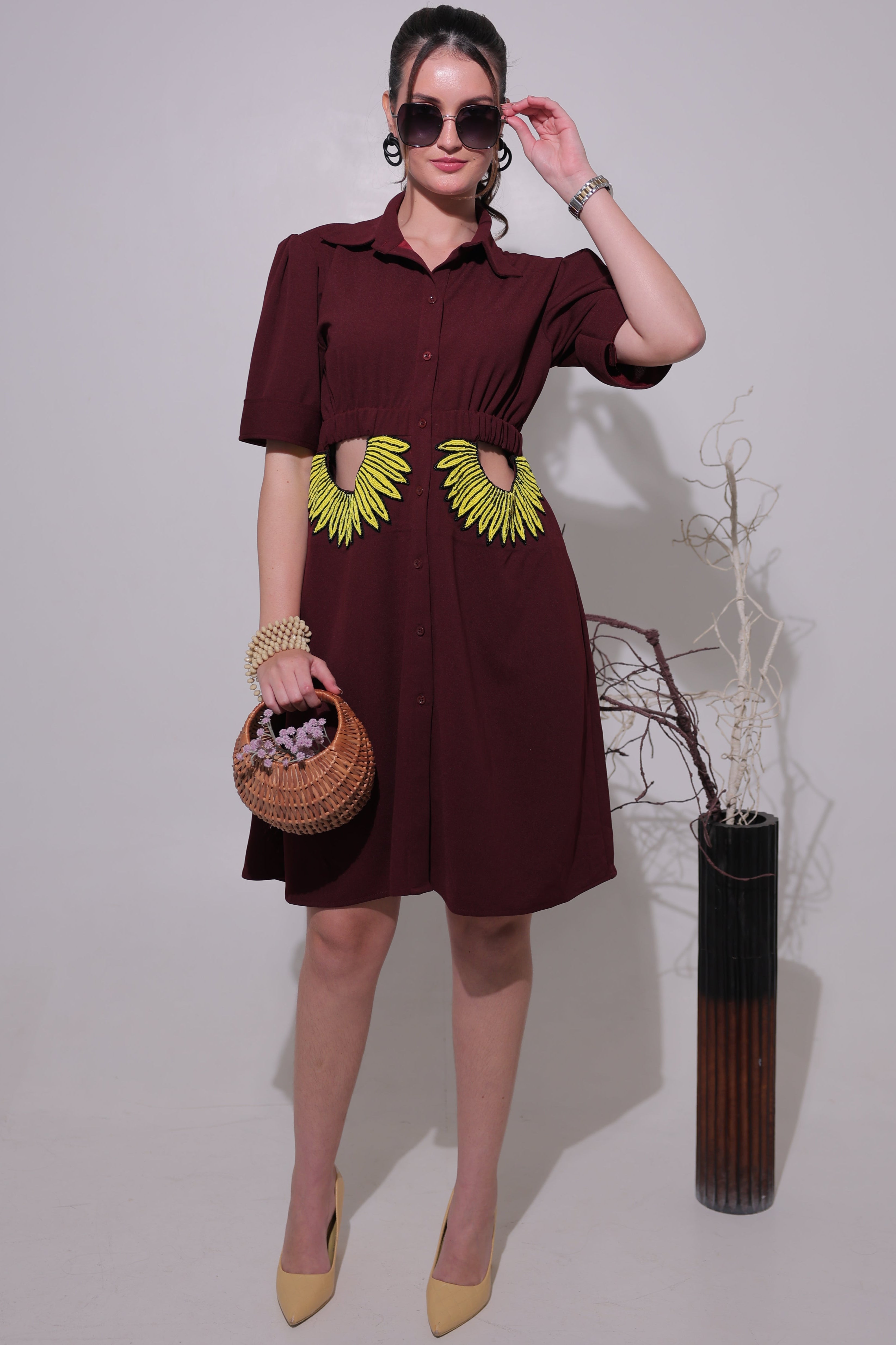Woman in a maroon dress with yellow accents holding a woven basket on a plain background