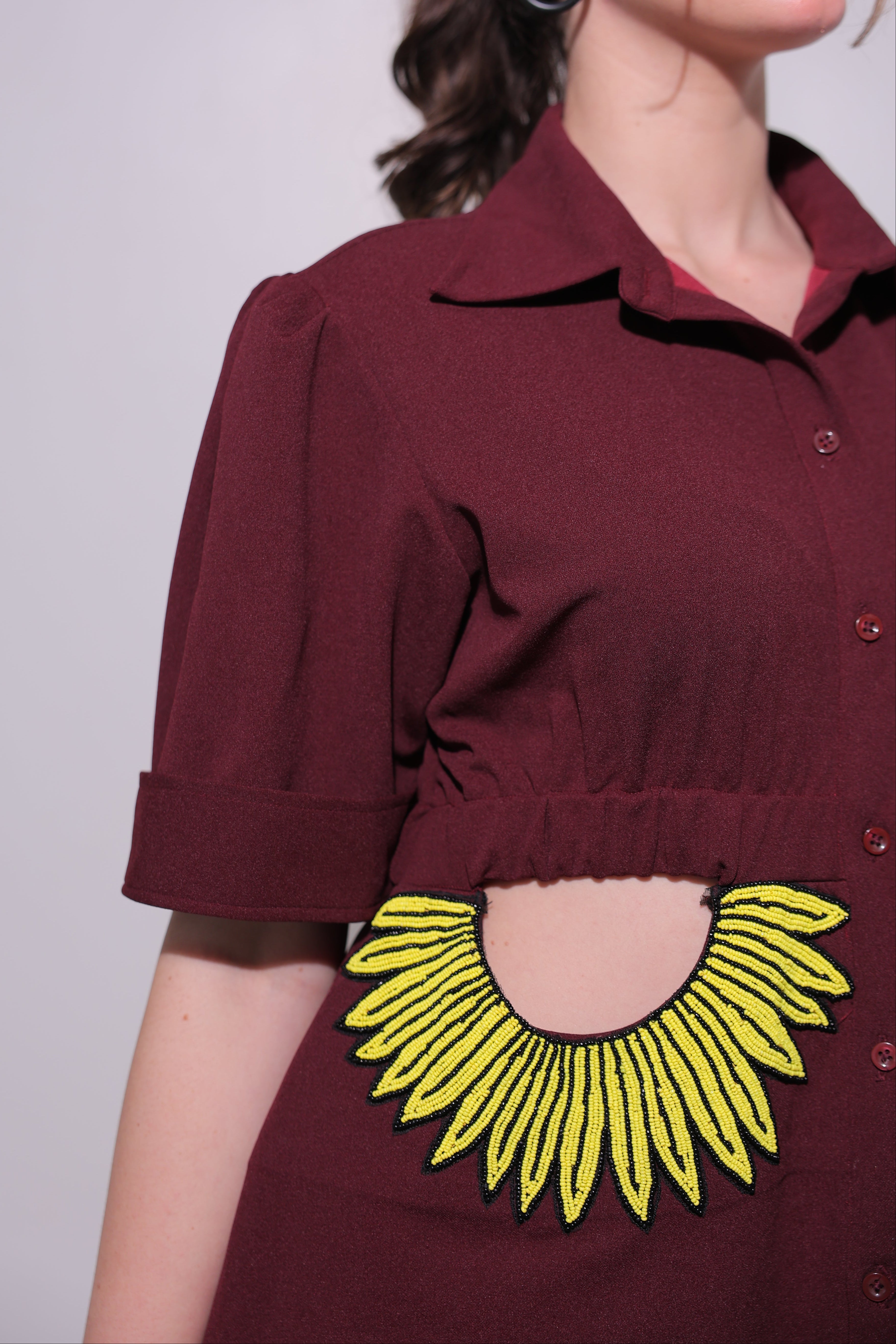Close-up of a maroon dress with a yellow floral design on a plain background