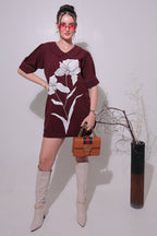 Person wearing a maroon dress with floral patterns, standing against a plain background.