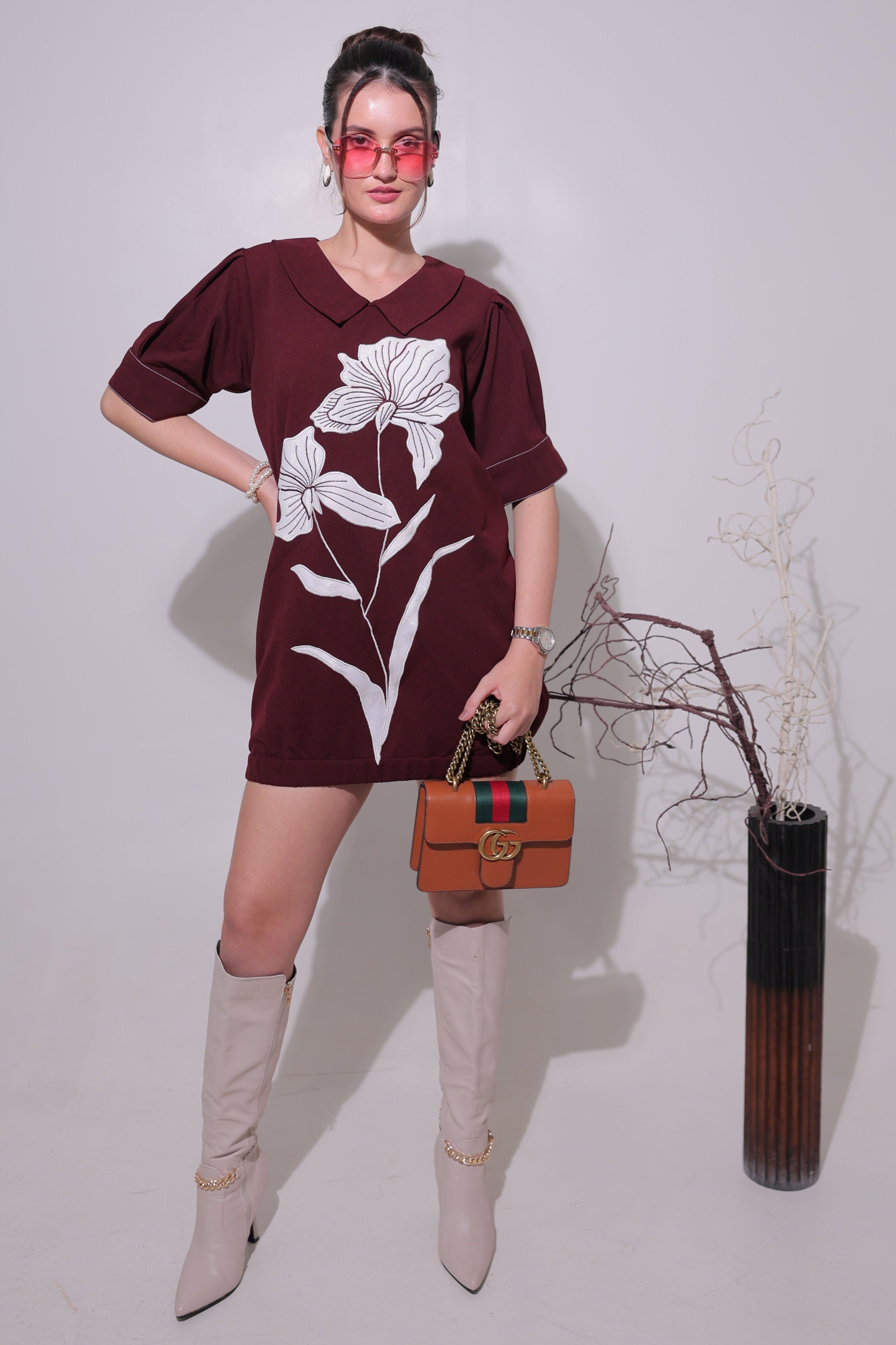 Person wearing a maroon dress with floral patterns, standing against a plain background.