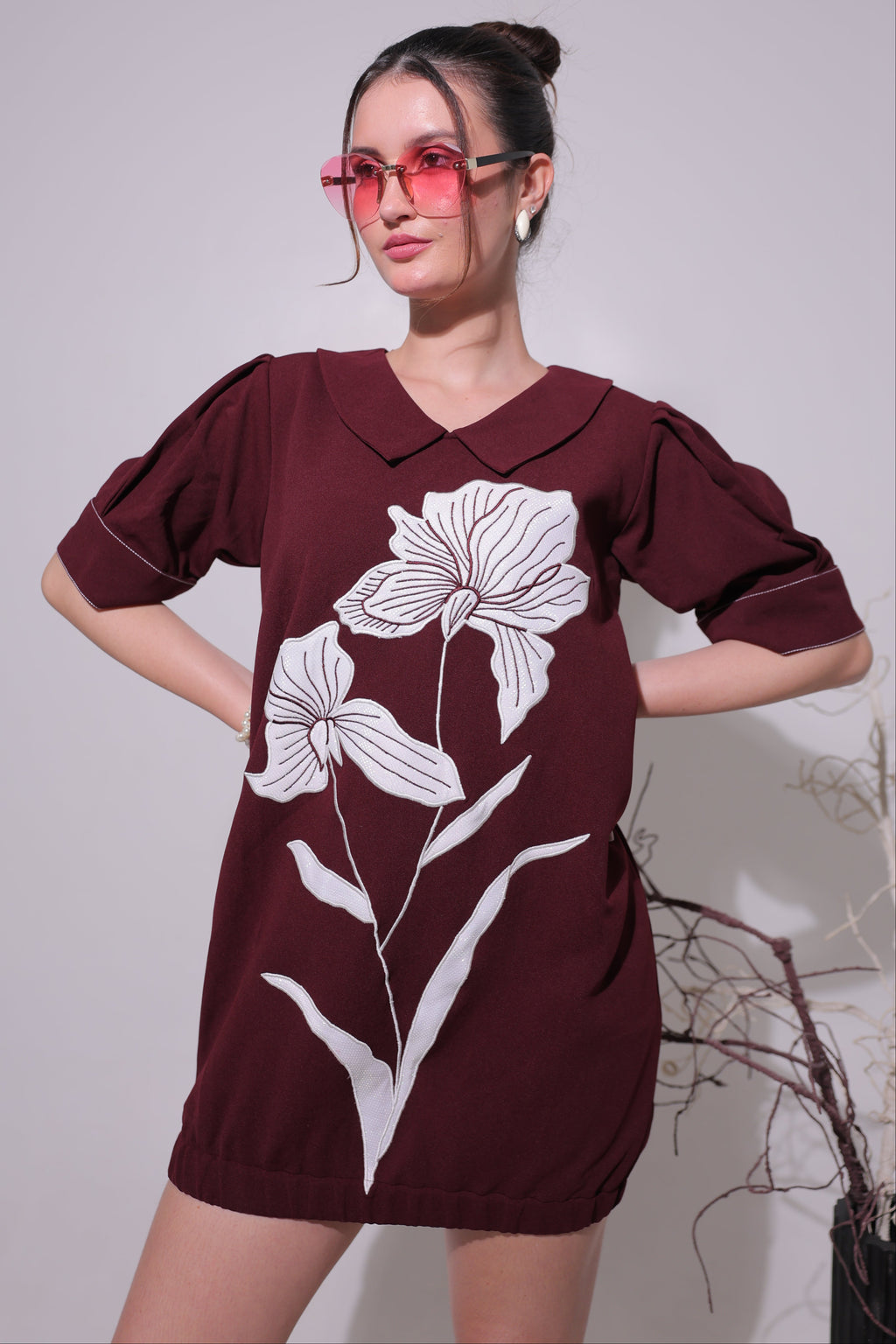 Woman wearing a maroon dress with white floral patterns against a plain background