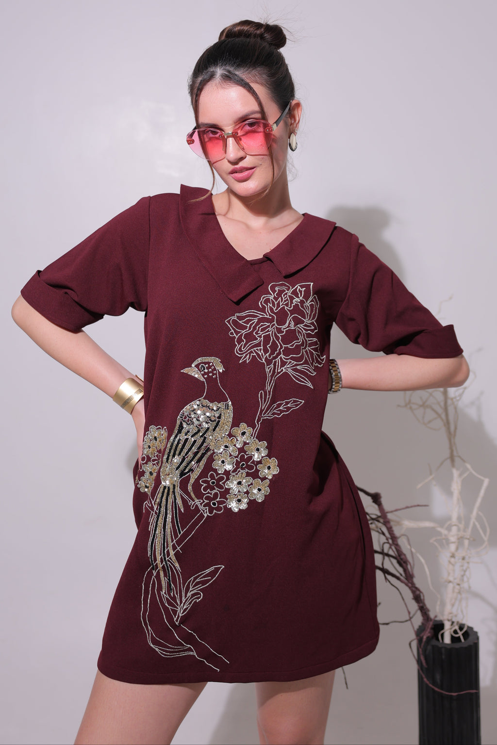 Woman wearing a maroon dress with floral embroidery on a plain background