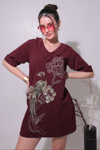 Woman wearing a maroon dress with floral embroidery on a plain background