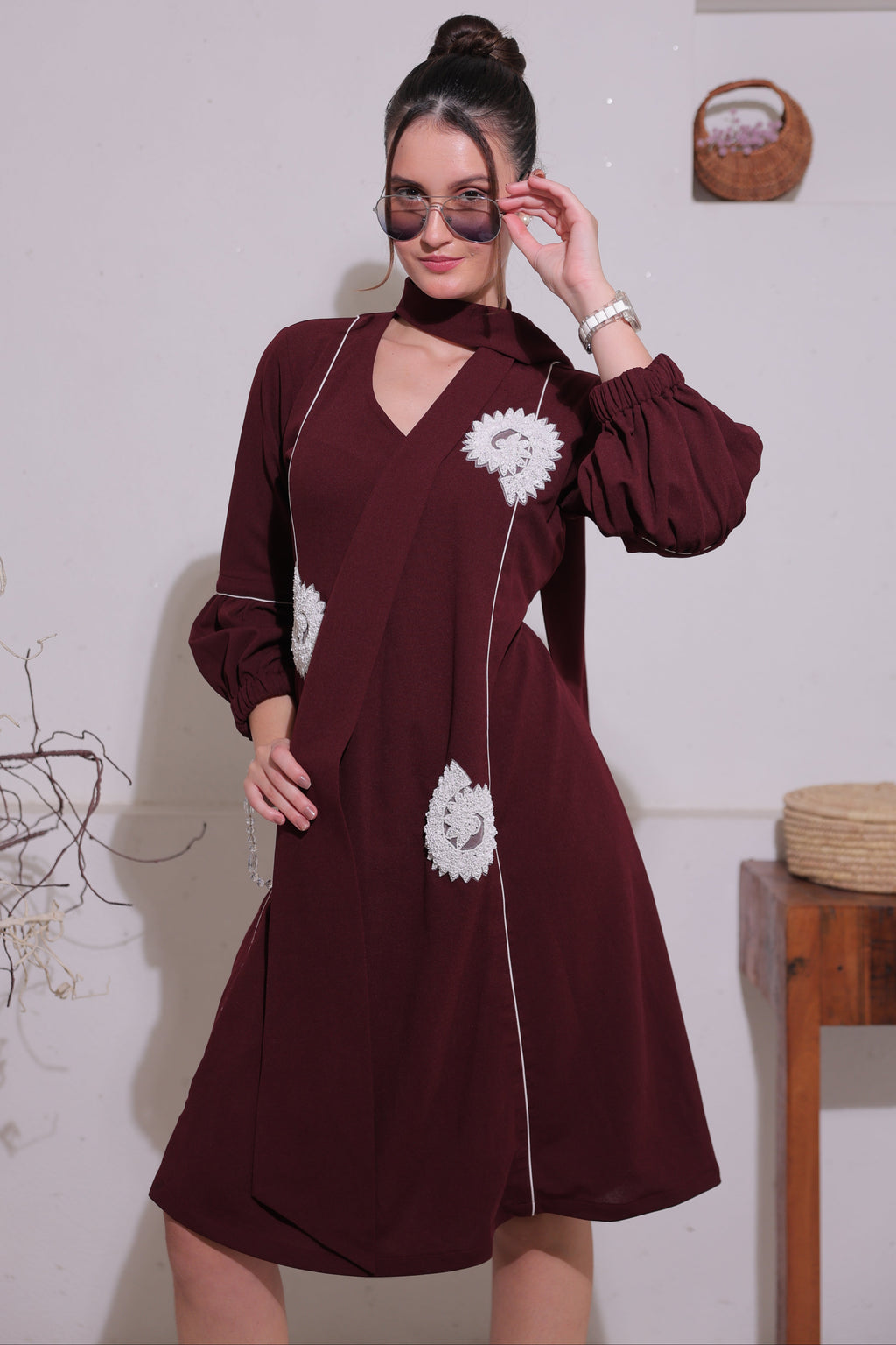 A woman wearing a maroon dress with white floral patterns on a plain background