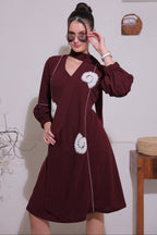 A woman wearing a maroon dress with white floral patterns on a plain background