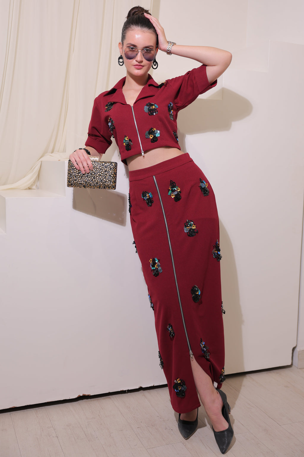 A woman in a maroon dress with black embellishments is posing indoors.