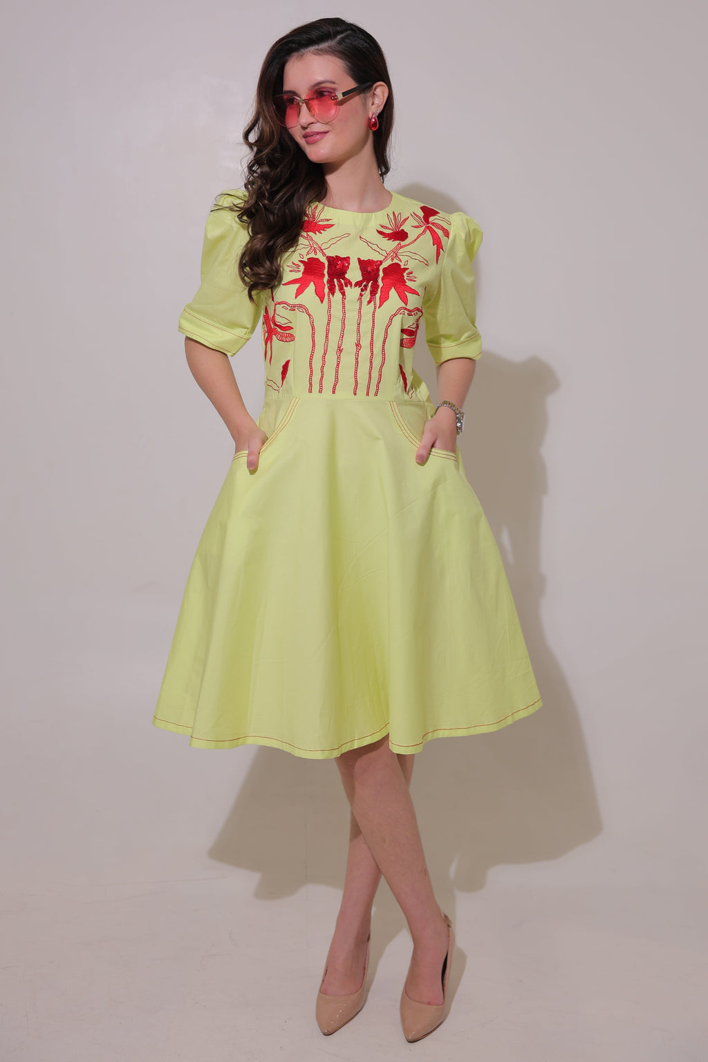 Woman wearing a lime green dress with red floral patterns on a plain background