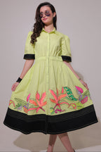 Woman wearing a lime green dress with floral embroidery on a plain background