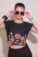 Woman wearing a black top with red floral patterns and sunglasses against a plain background